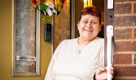 A Tenant Standing Outside Against Their Yellow Door, Holding A Handrail And Smiling