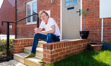 Man Sitting On The Stairs Outside Of His Home Entrance On A Sunny Day