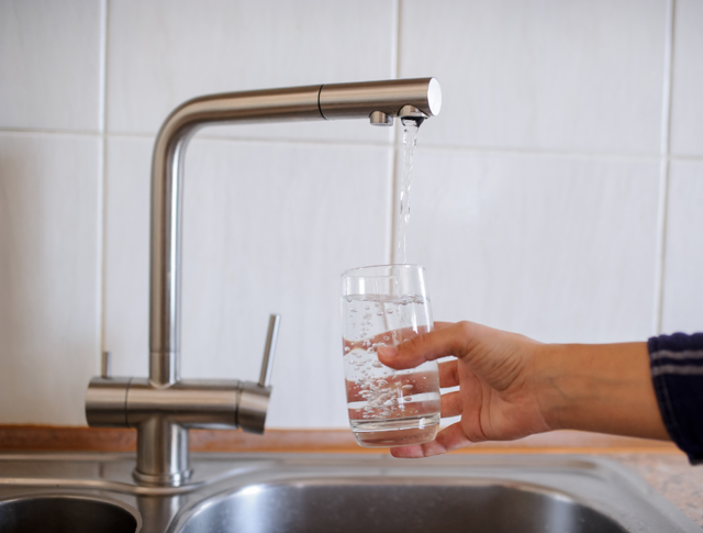 A person pouring a glass of water from the tap