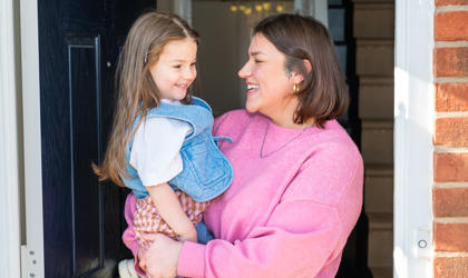 A Mother Holding Her Daughter In The Doorframe Of Their Home