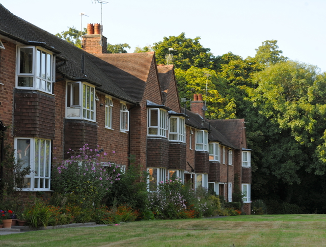 A row of houses with grass in the front and trees in the background