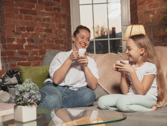 Mother and daughter drinking out of mugs, sitting on a sofa