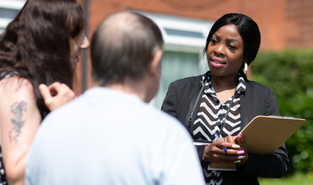 A Midland Heart employee with a clipboard speaking to 2 tenants