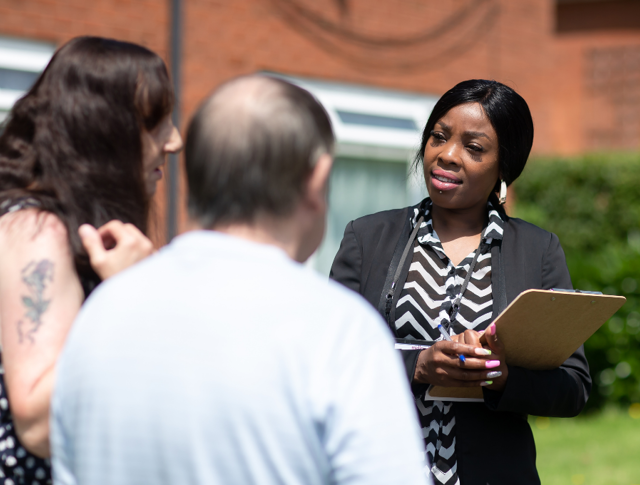 A Midland Heart employee with a clipboard speaking to 2 tenants