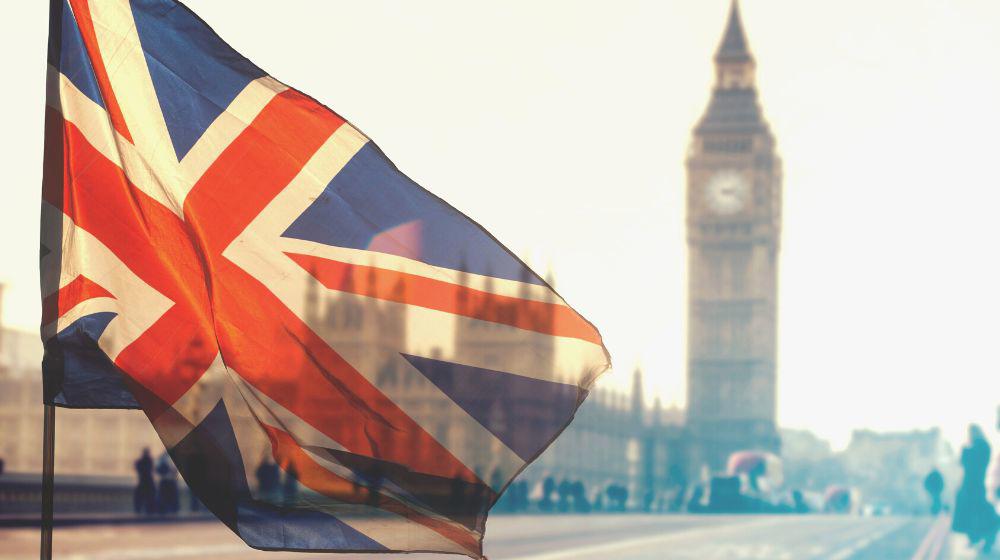 A UK flag floating in the wind with Big Ben in the background