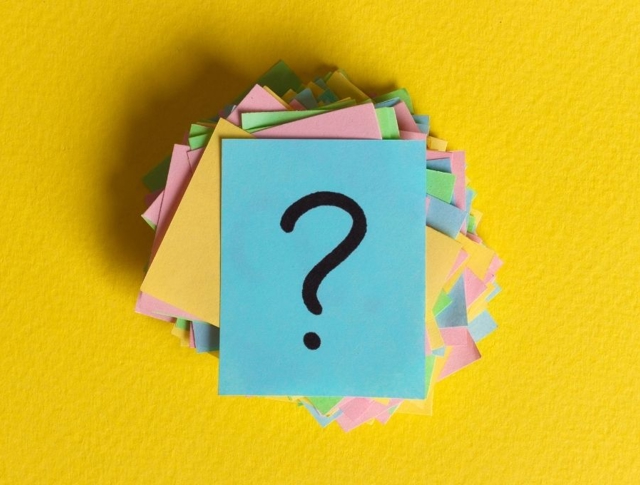 Post-it notes in a pile with the top one having a question mark written on it