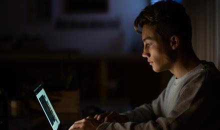 A young man staring at his laptop in the dark