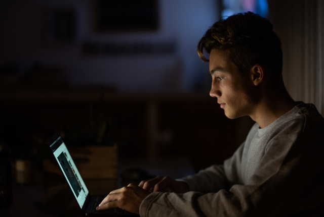 A young man staring at his laptop in the dark