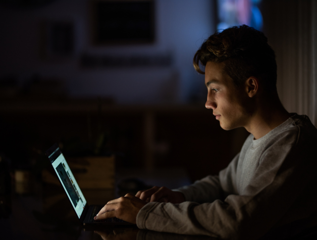 A young man staring at his laptop in the dark